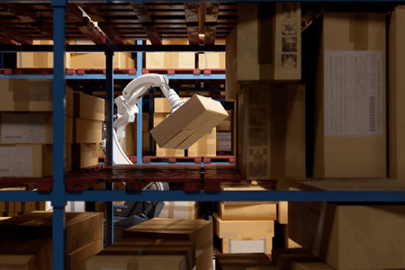 Robotic arm handling a box between warehouse shelves